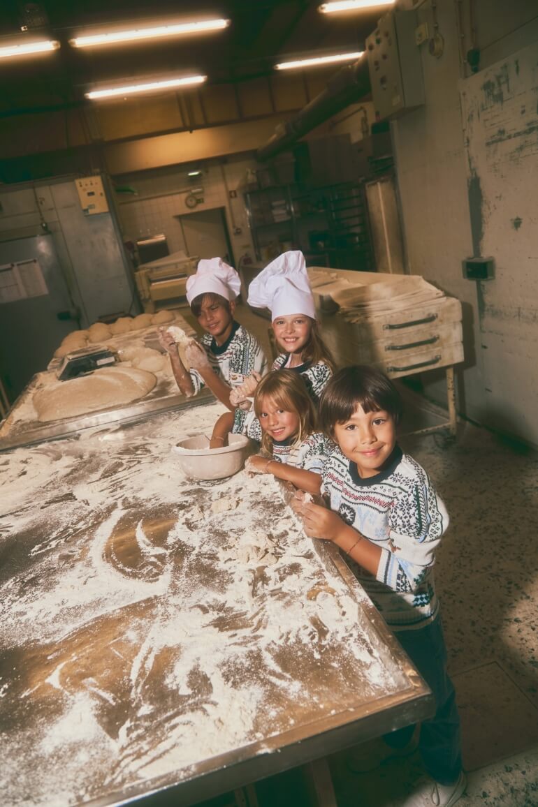 Crianças a cozinhar numa padaria, mesa coberta de farinha